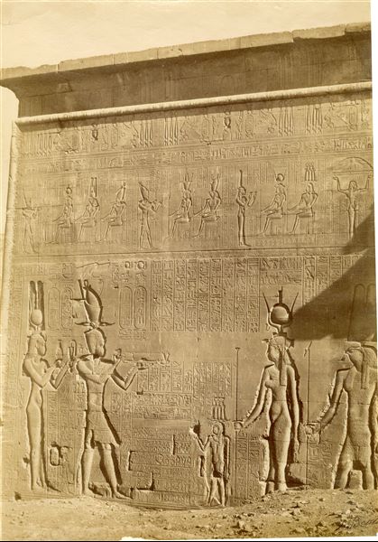 View of a sacred relief scene on the outer (southern) wall of the Temple of Hathor at Dendera, where Cleopatra VII and Ptolemy XV Caesarion (left) perform rituals to honour the gods Harsomtu (depicted smaller), Isis, Harsomtu and other deities are not visible in this image. The author's signature is visible at the lower right.  