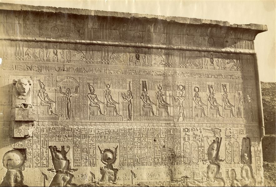 L’immagine mostra il dettaglio della decorazione parietale esterna del lato meridionale del Tempio di Hathor a Dendera, ancora parzialmente coperto dal terreno.