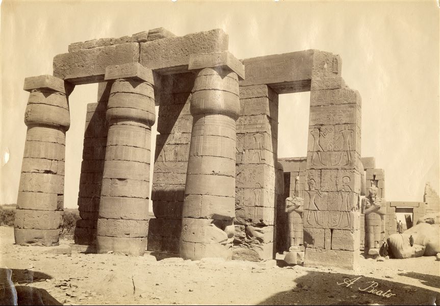 View of some columns from the Ramesseum in West Thebes, built by Pharaoh Ramesses II. In the background, two of the collossal Osiride pillars of Ramesses II are visible, which are still standing, and other statues of even more monumental dimensions are lying on the ground. The author's signature is clearly visible at the bottom right.