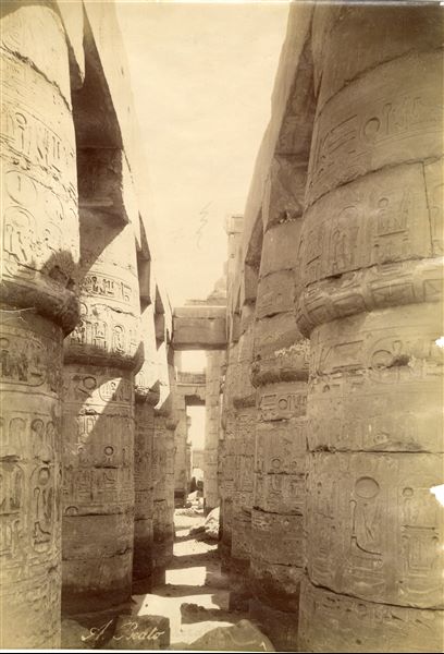 La fotografia ritrae un intercolumnio laterale all'interno della Grande Sala Ipostila del complesso templare di Amon a Karnak, costruita dal faraone Seti I, della XIX Dinastia. In basso, è apposta la firma dell'autore.