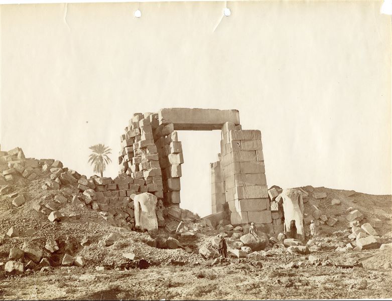 The picture shows the northern side of the tenth pylon in the Karnak Temple Complex, built by Pharaoh Horemheb with two colossal statues of the pharaoh (later reused by Ramesses II) on either side of the gate, the only architectural element of the pylon still visible. The presence of some egyptians give an idea of the large size of the monument. The author's signature is visible at the bottom right. 