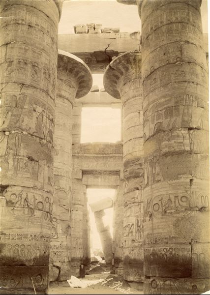 The photograph shows a view of the colonnade, with papyrus columns not yet completely cleared of sand, from the Great Hypostyle Hall of the Karnak Temple Complex. The author's signature is at the bottom.   