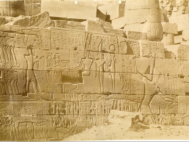 Veduta di una parte della parete settentrionale esterna della Grande Sala Ipostila del complesso templare di Amon a Karnak, costruita dal faraone Seti I: si riconosce il faraone durante le campagne militari (a destra) e mentre dedica la vittoria sui nemici ad Amon (in alto a sinistra). La firma dell’autore è posta in basso al centro.