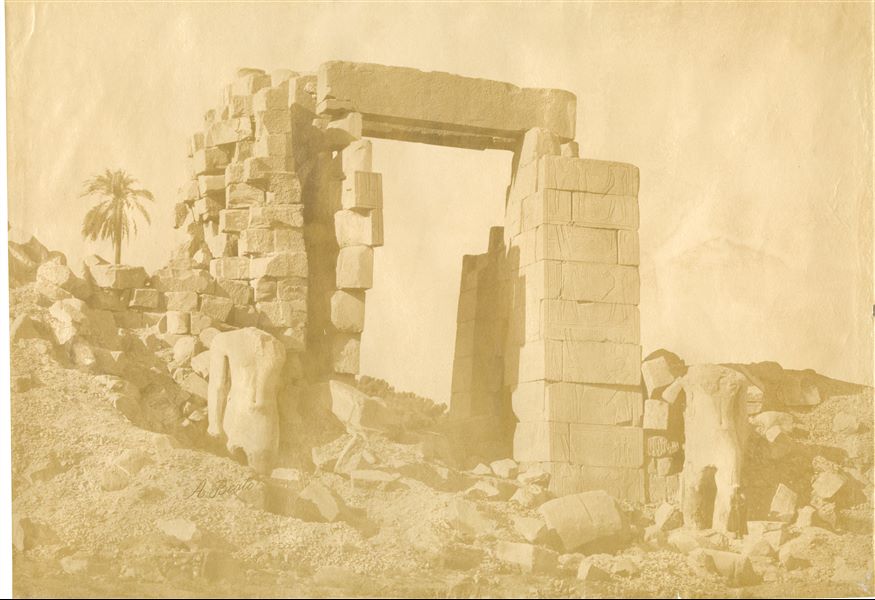 La fotografia presenta il lato settentrionale del X pilone, ancora da restaurare, nel complesso templare di Amon a Karnak, costruito dal faraone Horemheb, con due statue colossali del faraone (poi riutilizzate da Ramesse II) ai lati del portale. Il livello del suolo copre ancora la parte inferiore dei colossi. La firma dell'autore è posta in basso a sinistra.  