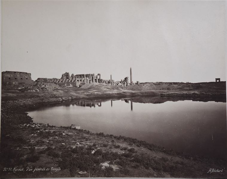 General view of the main axis of the Karnak Temple Complex, including the columns of the Great Hypostyle Hall, photographed from the Sacred Lake. Between the Sacred Lake and the Great Hypostyle Hall, the remains of the seventh pylon can be seen. The author's signature is visible at the lower right.