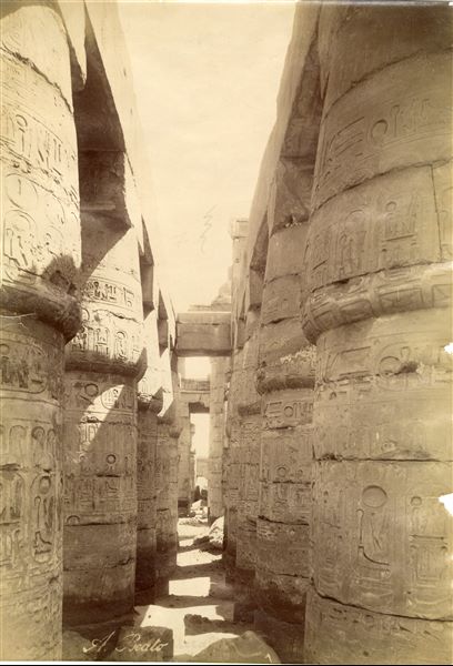 The photograph depicts a lateral intercolumniation within the Great Hypostyle Hall of the Karnak Temple Complex, built by Pharaoh Seti I in the 19th dynasty. The author's signature is at the bottom. 