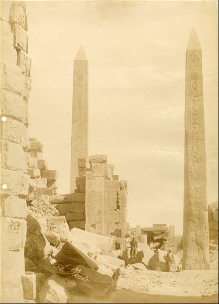The photograph shows a close view from the south of the area built by Pharaoh Tuthmosis I in the Karnak Temple Complex. The obelisk of the pharaoh (right) and that of Hatshepsut (left) are visible. The author's signature is at the bottom left. 