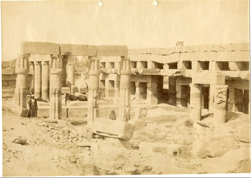 In the image there are some Egyptians among the ruins of the Akhmenu (“Festival Hall”), the temple built by ruler Tuthmosis III within the Karnak Temple Complex. Among the ruins, four papyrus columns are still standing. The photograph can be attributed to Antonio Beato. 