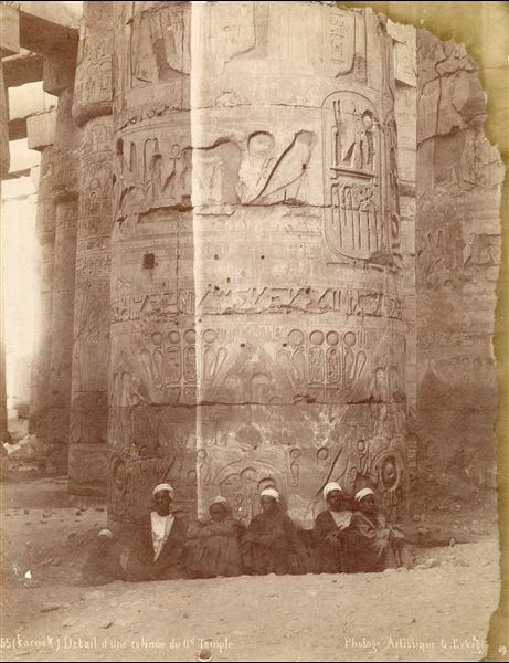 La fotografia ritrae sei giovani egiziani davanti ad una colonna nella Grande Sala Ipostila del complesso templare di Amon a Karnak, con il cartiglio del faraone Ramesse II. In basso, la firma dell'autore.