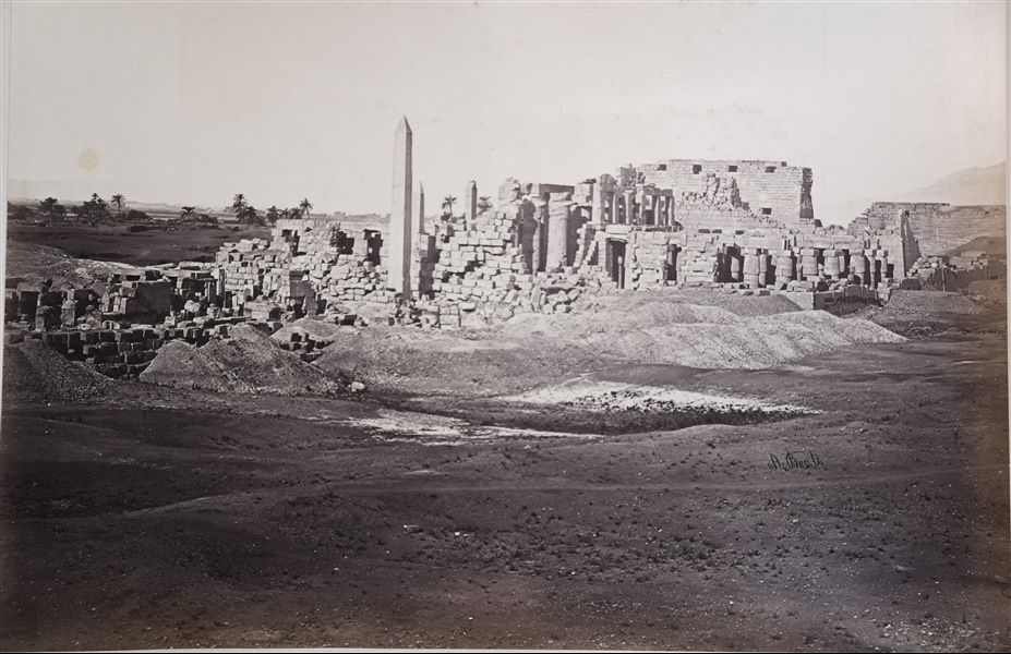 View of a part of the Karnak Temple Complex. Standing out in the centre are the remains of the Wadjet Hall, the Great Hypostyle Hall, and behind it, the remains of the second pylon. On the left, there are two obelisks, one erected by Tuthmosis I, the other by Queen Hatshepsut. The Nile can be seen in the background. The author's signature is on the right.