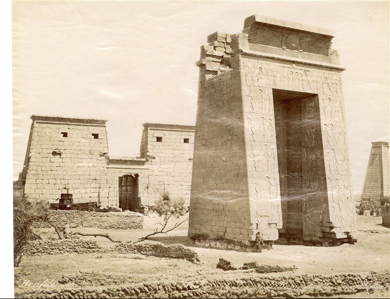 The photograph shows the southern gate built by Ptolemy III, and behind it, the pylon of the Temple of Khonsu inside the Karnak Temple Complex. The author's signature is visible at the bottom left. 