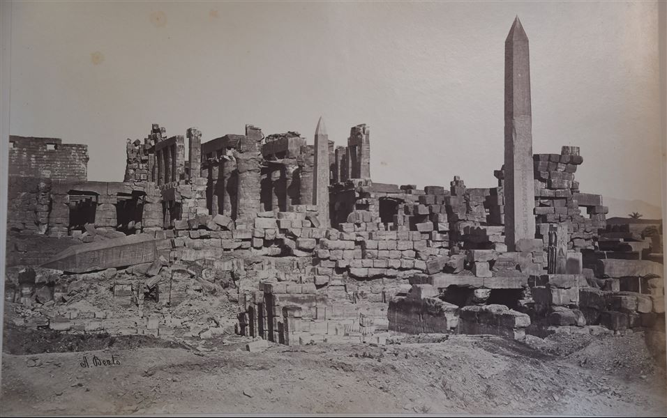 View of the remains of the Great Hypostyle Hall, where three obelisks are clearly visible, two still standing (one of Tuthmosis I, centre, the other of Hatshepsut, right) and one collapsed (also belonging to Queen Hatshepsut), due to an earthquake during the Middle Ages. The author's signature is visible at the bottom left. 