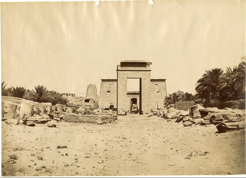 The photograph was taken in the direction of the Avenue of the Sphinxes with ram's heads, facing towards the Temple of Khonsu at Karnak. The southern gate of the sacred enclosure of the Karnak Temple Complex and the entrance to the Temple of Khonsu can be made out. The author's signature is visible at the bottom. 