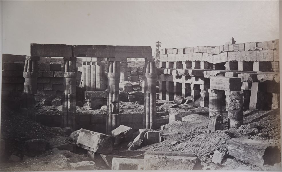 L'immagine mostra le rovine dell’Akhmenu (la “Sala delle Feste”), il tempio costruito dal sovrano Thutmosi III nel complesso templare di Amon a Karnak. Tra le rovine, spiccano quattro colonne papiriformi ancora stanti. La firma dell’autore si trova in basso.  