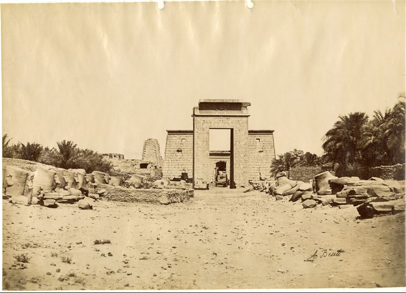 La fotografia è stata scattata in direzione dal Viale delle sfingi a testa di ariete guardando verso il tempio di Khonsu a Karnak. Si distinguono la porta meridionale della cinta sacra del complesso templare di Amon e l'accesso al tempio di Khonsu. In basso, la firma dell’autore. 