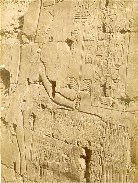 Dettaglio della decorazione della parete settentrionale esterna della Grande Sala Ipostila ramesside del complesso templare di Amon a Karnak. Il faraone Seti I è rappresentato nell'atto di abbattere i nemici Retenu (sconfitti durante la campagna palestinese). In basso a sinistra è posta la firma dell’autor
