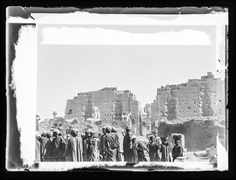  In the foreground, a group of Egyptians near the eighth pylon of the Karnak Temple Complex, with the Hypostyle Hall in the background. 19th century photograph.