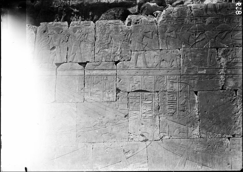 South side of the mortuary temple of Queen Hatshepsut at Deir el-Bahari. Wall scene from the portico in the middle terrace. In the upper register there is a scene of tribute and in the lower, the Egyptian fleet is departing from Punt. Wall photographed before it was restored.  