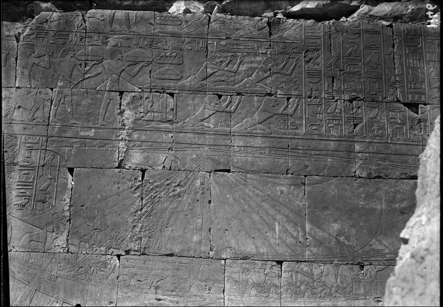 South side of the mortuary temple of Queen Hatshepsut at Deir el-Bahari. Wall scene from the portico in the middle terrace. In the upper register there is a scene of tribute and in the lower, the Egyptian fleet. Wall photographed before it was restored.  
