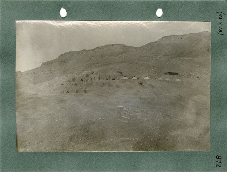Photograph of the village of Deir el-Medina, just visible in the foreground, and view of the Italian Mission’s camp, consisting of six conical tents, and a small brick building with a veranda, on the upper level of the slope. In the background, there is the mountain of Deir el-Medina, where numerous rock-cut tombs were built. Schiaparelli excavations 