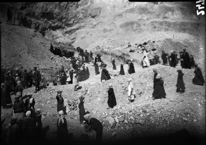 Excavations to the right of the temple, up the mountain slope. The employment of a large number of workers was necessary to systematically assess the soil until the ancient stratigraphic layer was reached. In the centre of the picture there is a pole that indicates the next area to be excavated, with special precautions. Visible on the left of the image is Benvenuto Savina.   Schiaparelli excavations. 
