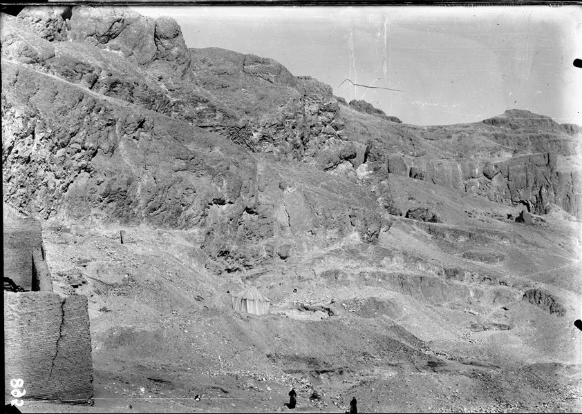 View of the archaeological area to the right of the temple of the goddess Hathor. On the lower left, the enclosure wall of the temple is visible. In the centre there is a tent, not belonging to the members of the mission but probably to the local guards. At the bottom, there are two Franciscan friars from the nearby missionary station of Luxor. Schiaparelli excavations. 