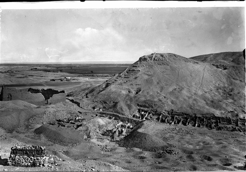 Veduta generale dell’area di Deir el-Medina. La foto è stata scattata dalla montagna a occidente, in basso si vedono le prime case del villaggio con, a sinistra, il tempio della dea Hathor. Di fronte la montagna orientale che delimita il sito, sulla sinistra si intravedono spuntare le rovine del Ramesseo con i suoi magazzini; sullo sfondo la pianura coltivata fino a raggiungere il Nilo. Scavi Schiaparelli. 
