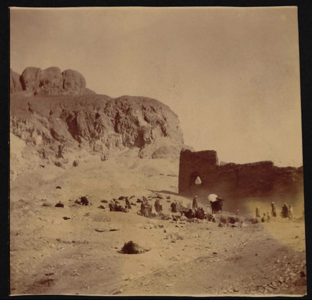 Excavating in front of the temple of Hathor in the village of Deir el-Medina. Among the people photographed, one can be seen from behind with an open parasol, they type often used by Schiaparelli during excavations. Schiaparelli excavations. 