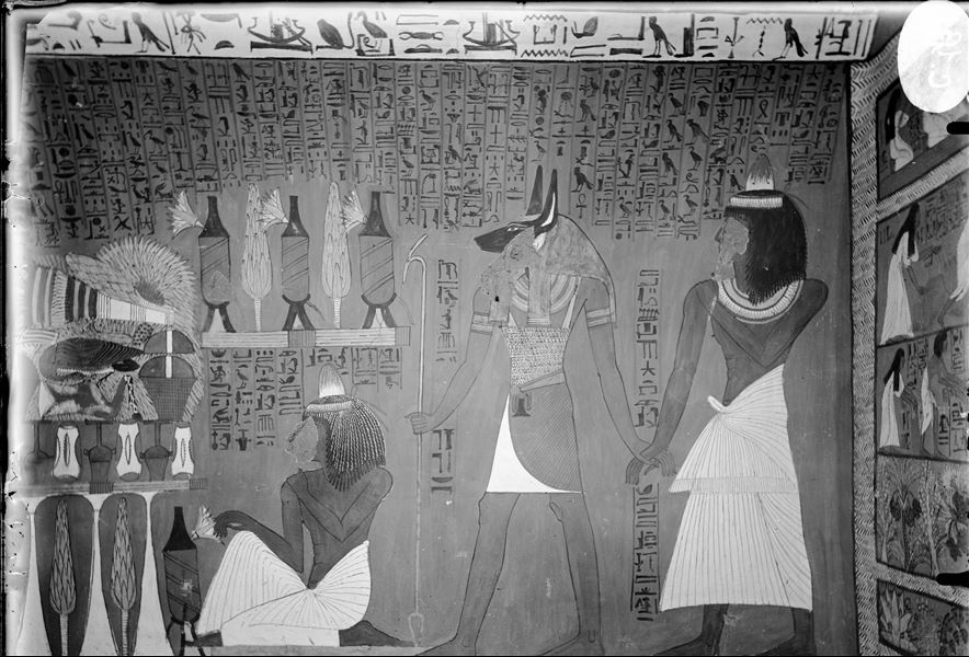 North wall (back) from the tomb of Sennedjem (TT1). On the right, the god Anubis leads the deceased by the hand. The text accompanying the scene describes Anubis’ guidance of the deceased in front of the gods of the Duat. In the centre, Sennedjem is kneeling in front of a pile of offerings in honour of the god Osiris (who is on the left but not visible in this photograph). 