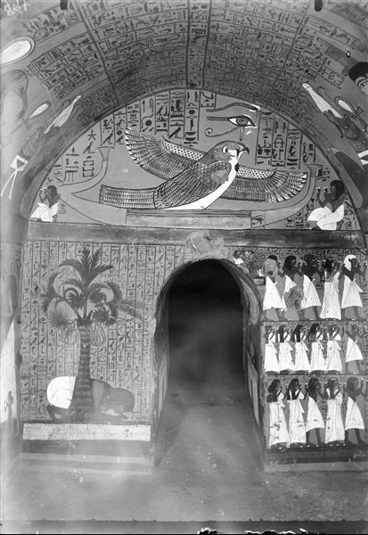 East wall (of the entrance) from the burial chamber of the tomb of Pashedu (TT 3). The upper register shows Ptah-Sokar in the form of a falcon, on a solar barque. Below, on either side of the entrance: on the left, the deceased stands under a palm tree, drinking water and on the right, three registers depicting relatives of the deceased, with the presence of a deity in the form of a tree. 