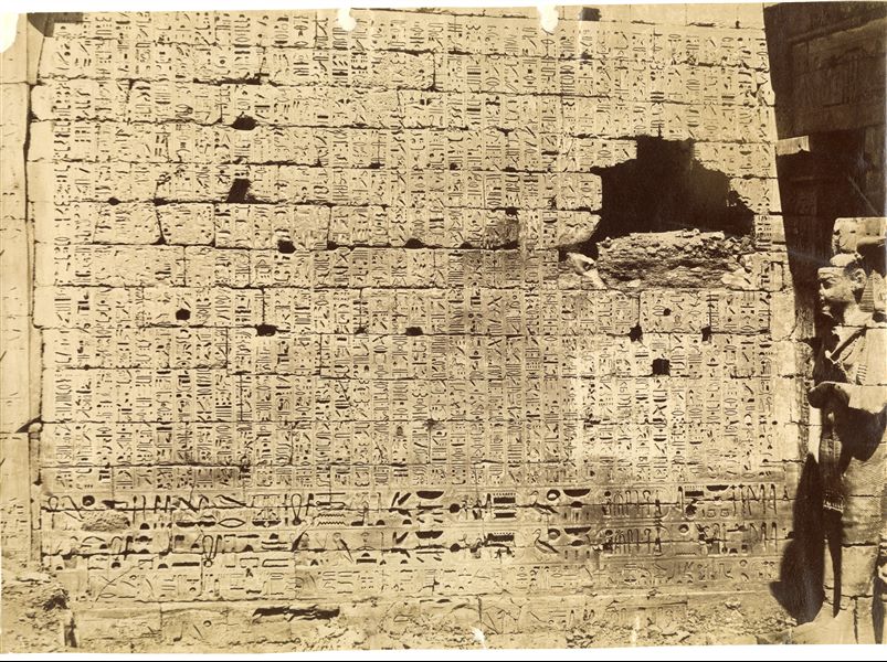 The photo shows a close-up of the texts on the second pylon from the Temple of Ramesses III at Medinet Habu, photographed from the first courtyard. One of the colossal Osiride pillars of the colonnade to the north can also be seen on the right. 