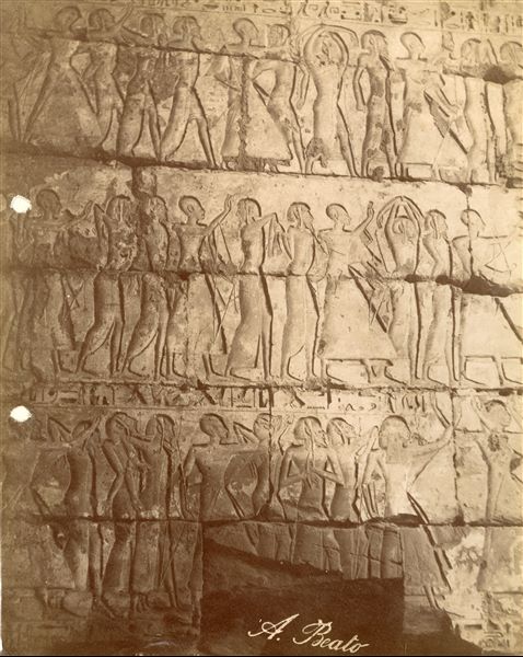 La fotografia riprende un dettaglio della decorazione a bassorilievi della parete interna, muro sud, del secondo cortile del tempio funerario di Medinet Habu, costruito da Ramesse III: tre teorie di prigionieri libici sfilano verso il Faraone (non inquadrato) condotti da soldati egiziani.  