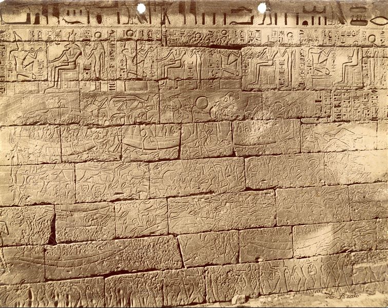 The photograph shows a naval battle from the northern outer wall of the Funerary Temple of Pharaoh Ramesses III at Medinet Habu. The Sea Peoples can be identified, being defeated by the Egyptians. In the upper register, Pharaoh Ramesses III performs offering rituals to honour various deities. The author's signature is at the bottom right. 