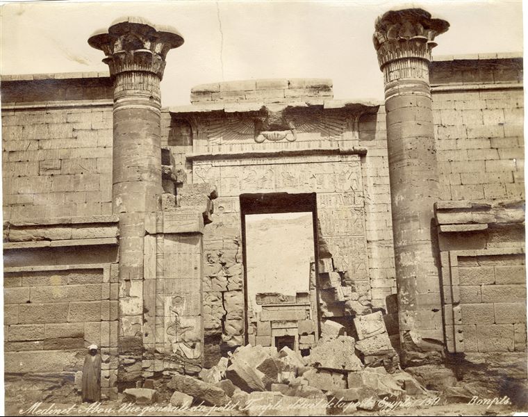 Nella fotografia è rappresentato l’ingresso nel primo cortile del cosiddetto Tempio minore, della XVIII dinastia, all’interno del recinto del tempio di Medinet Habu, sulla riva occidentale del Nilo, a Tebe Ovest, costruito dal faraone Ramesse III, della XX dinastia. Fotografia scattata prima dei lavori di pulizia e restauro. In basso a destra la firma dell’autore.  