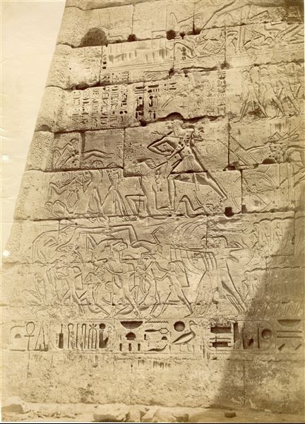 La fotografia ritrae alcune scene di guerra sulle pareti esterne del tempio funerario di Ramesse III a Medinet Habu, contro I Libici (esterno I pilone, torre nord, lato ovest). In basso a destra si legge la firma dell'autore, a specchio.  