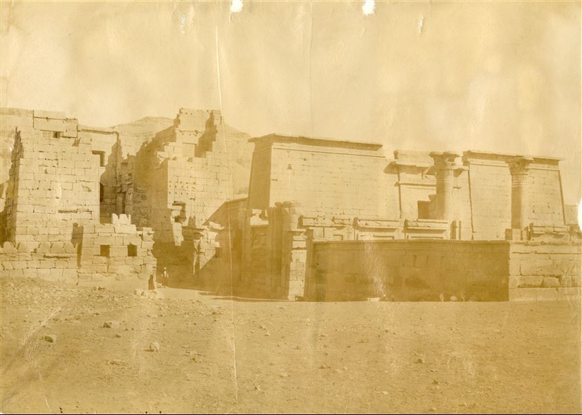 The photograph depicts an overall view of the entrance to the Temple of Medinet Habu, built by Ramesses III. In particular, on the left is the migdol -  the architectural structure reminiscent of a syrian fortress, while on the right, is the smaller temple from the 18th Dynasty, which was later incorporated into the Medinet Habu complex. The image can be attributed to Antonio Beato. 