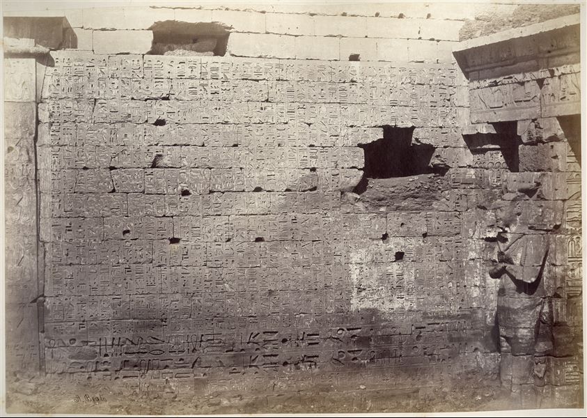 Fotografia della parete anteriore del II pilone del tempio di Medinet Habu. Sulla destra si nota uno dei pilastri osiriaci. In basso a sinistra si trova la firma dell’autore.  