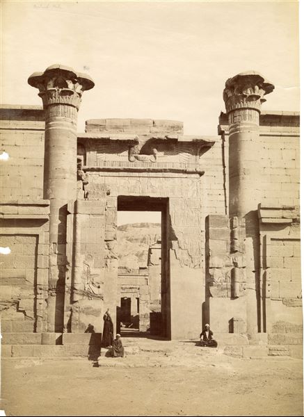 The photograph shows three locals standing in front of the entrance to the so-called “Small Temple” from the 18th Dynasty, within the enclosure of the temple of Medinet Habu in West Thebes, built by the 20th Dynasty Pharaoh Ramesses III. The entrance gates, however, were built in the Late and Ptolemaic Periods. Photograph taken after the cleaning and restoration of the gate. The author's signature is at the bottom left, in mirror image. 