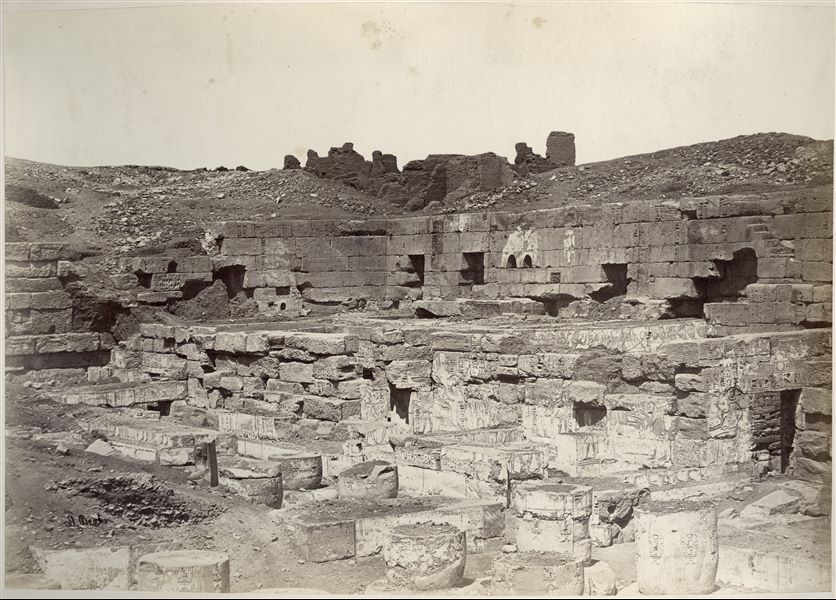 Veduta della seconda corte del tempio di Medinet Habu, costruito dal faraone Ramesse III sulla riva ovest del Nilo, a Tebe. Si notano ancora numerose colonne a terra, e le colonne papiriformi stanti ancora parzialmente interrate, indizi che dimostrano la data dello scatto, prima dei lavori di pulizia e restauro del sito. In basso a sinistra si trova la firma dell’autore.  
