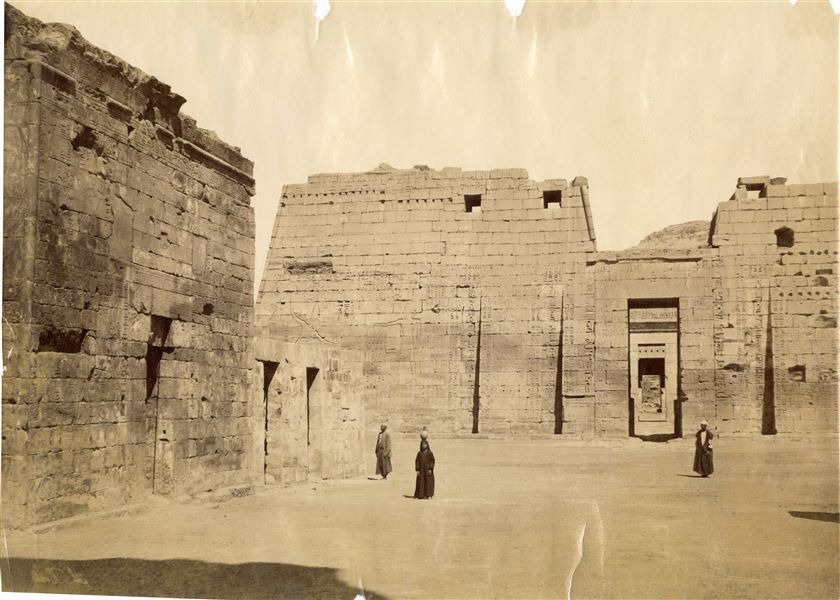 The photograph shows the first pylon of the Temple of Ramesses III at Medinet Habu, in an axial view (along the axis, the second pylon and the innermost rooms are visible). The author's signature is written in mirror image at the bottom left. 