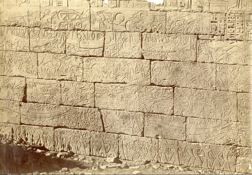 La fotografia illustra varie fasi del combattimento che impegnò la flotta navale egiziana guidata da Ramesse III contro i Popoli del mare, scolpite in bassorilievo sulle pareti esterne del muro settentrionale del tempio di Medinet Habu sulla Riva Occidentale di Tebe. La firma dell’autore è posta in basso al centro, sottosopra.  