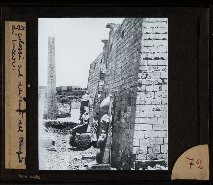 Accesso al tempio di Amon a Luxor fotografato lateralmente. Si riconoscono l'obelisco (a sinistra) e i colossi assisi e stanti (al centro) di Ramesse II.