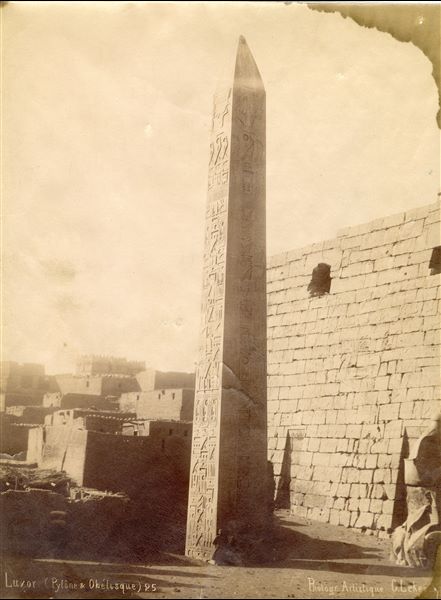 Nella fotografia è presentato l'obelisco orientale di Ramesse II davanti al pilone del tempio di Amon a Luxor (l’altro obelisco, quello occidentale, è attualmente a Place de la 
Concorde, a Parigi). Le parti inferiori dell’obelisco, del pilone e del colosso assiso del sovrano (il secondo colosso non è inquadrato) sono ancora parzialmente coperte di sabbia. Sullo sfondo si 
vede il villaggio ottocentesco di Luxor. In basso la firma dell’autore.