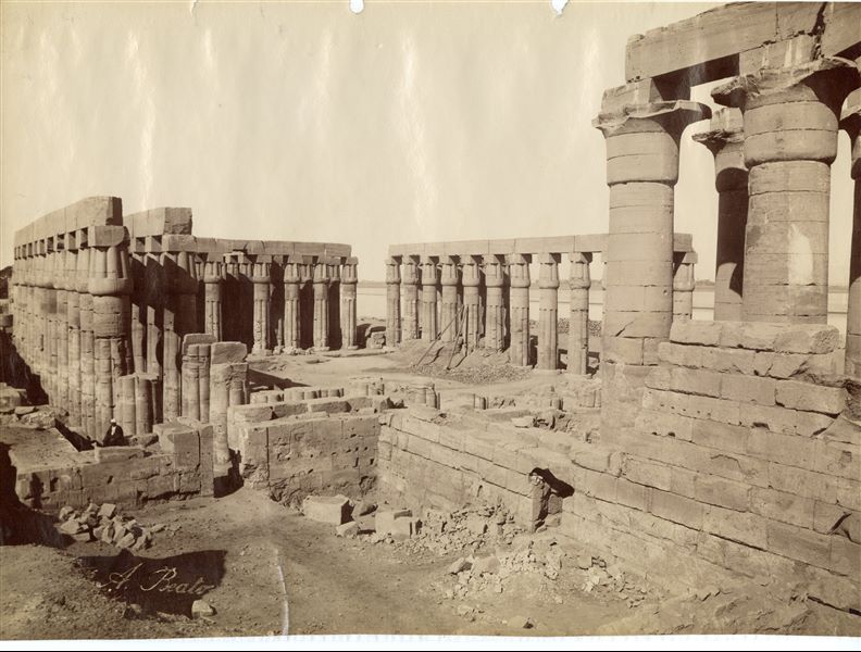 Veduta da nord-est del colonnato processionale di Amenhotep III e della corte anteriore del tempio di Amon a Luxor. Da notare che una delle colonne papiriformi della corte è puntellata in attesa di un consolidamento. In basso a sinistra la firma dell’autore. 