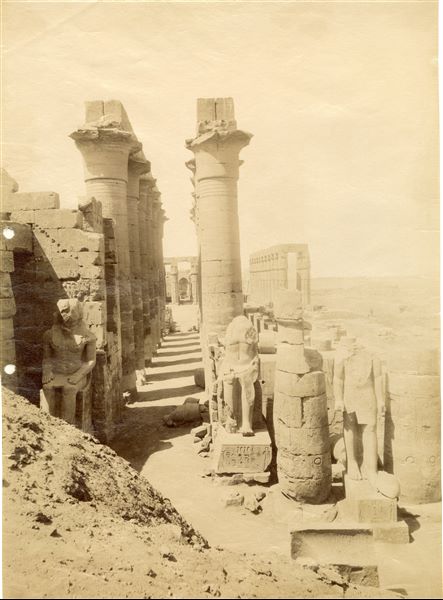 L’immagine rappresentata il colonnato processionale di Amenhotep III nel tempio di Amon a Luxor (guardando verso sud), che termina nel grande cortile anteriore al santuario. In primo piano, si notano le statue colossali assise di Ramesse II. La fotografia è posteriore a Inv15_003, come dimostra la mancanza di detriti ai piedi dei colossi.  