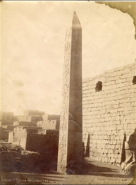 Nella fotografia è presentato l'obelisco orientale di Ramesse II davanti al pilone del tempio di Amon a Luxor (l’altro obelisco, quello occidentale, è attualmente a Place de la 
Concorde, a Parigi). Le parti inferiori dell’obelisco, del pilone e del colosso assiso del sovrano (il secondo colosso non è inquadrato) sono ancora parzialmente coperte di sabbia. Sullo sfondo si 
vede il villaggio ottocentesco di Luxor. In basso la firma dell’autore.