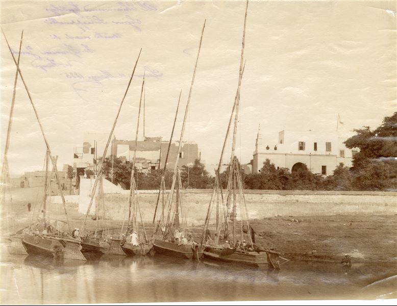 The photograph shows the building of the Franciscan Mission in Luxor, near the Temple of Luxor, on the terrace where a friar and a person in European dress stand. Behind, the pole with the Italian flag. In the foreground, several feluccas can be seen moored on the bank of the Nile. On the reverse of the image, there is an inscription written in blue pen in fine handwriting “Al Chiarissimo Egittologo Signor Schiapparelli [sic] Umile ricordo di F. Francesco Zanobi da Firenze. Luxor 11 Marzo 1885”, initialled below. The picture is attributable to Antonio Beato.