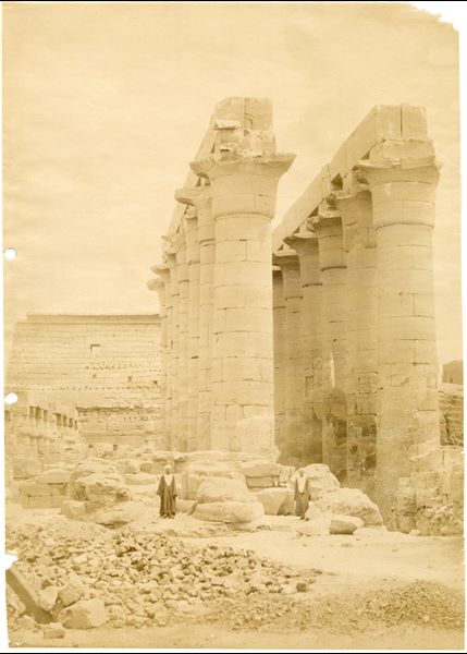 La fotografia rappresenta una veduta da sud-ovest del colonnato processionale di Amenhotep III nel tempio di Amon a Luxor, alla cui base si trovano due abitanti locali. Sullo sfondo si intravede il pilone di accesso al tempio eretto Ramesse II.  