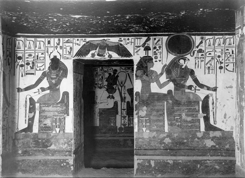 View of the east wall of the vestibule, from which there is access to the first eastern annex (alcove). From this area, the back wall of the vestibule can be seen. On the south side (right) of the wall, the gods Ra-Horakhty and Hathor are seated (scene 8). On the north side (left), the god Khepri is visible (scene 9). Above the access to the first eastern annex is the goddess Nekhbet in her animal form as a vulture. 
