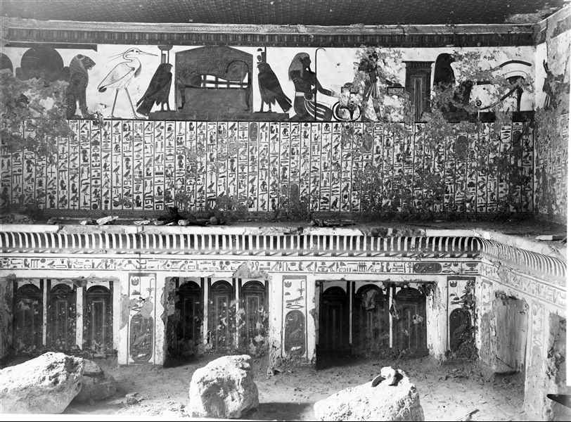 View of the antechamber, west wall, scene 3. Represented in the upper register: Atum between two lions, the Benu bird, the mummy (of Nefertari) on a bed between two falcons which represent the goddesses  Nephthys and Isis. These are representations connected with the central register, which presents Spell 17 of the Book of the Dead. Below, represented on the left is a decoration composed of Djed pillars and Tit knots, while in the centre there is a cavetto cornice, with representations of sanctuaries. The presence of wall fragments on the shelf and debris on the floor could suggest that the photograph was taken shortly after the discovery of the tomb.